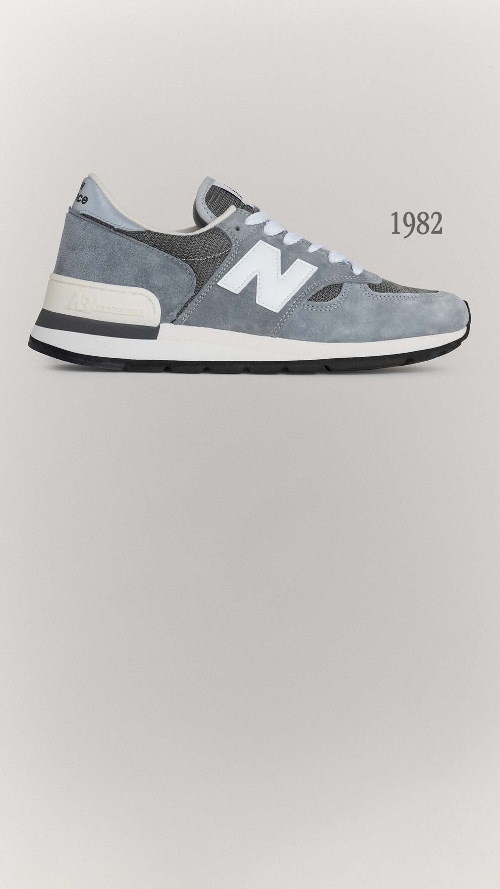 A grey 990v1 sneaker sitting on a grey background.