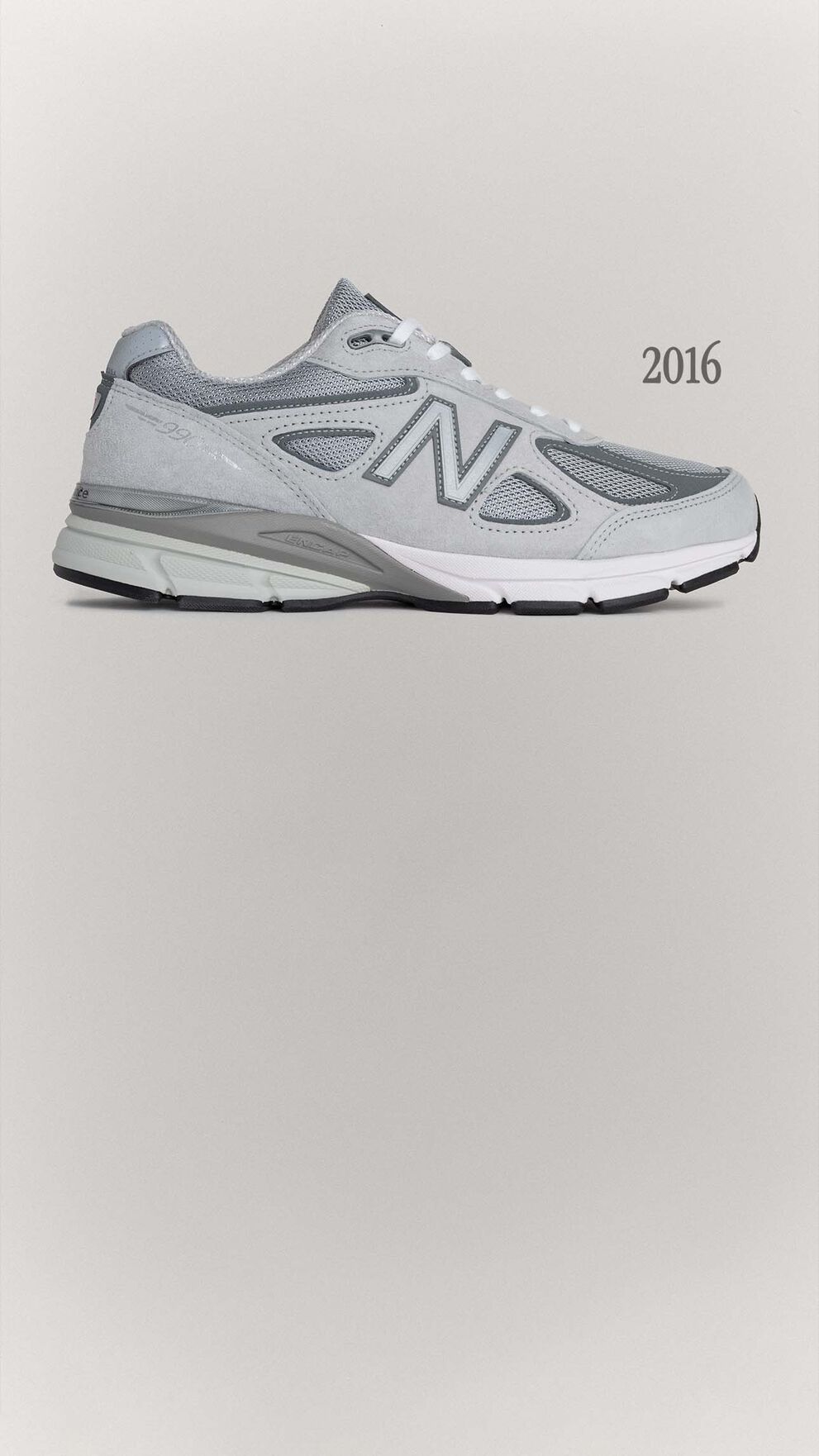 A grey 990v4 sneaker sitting on a grey background.