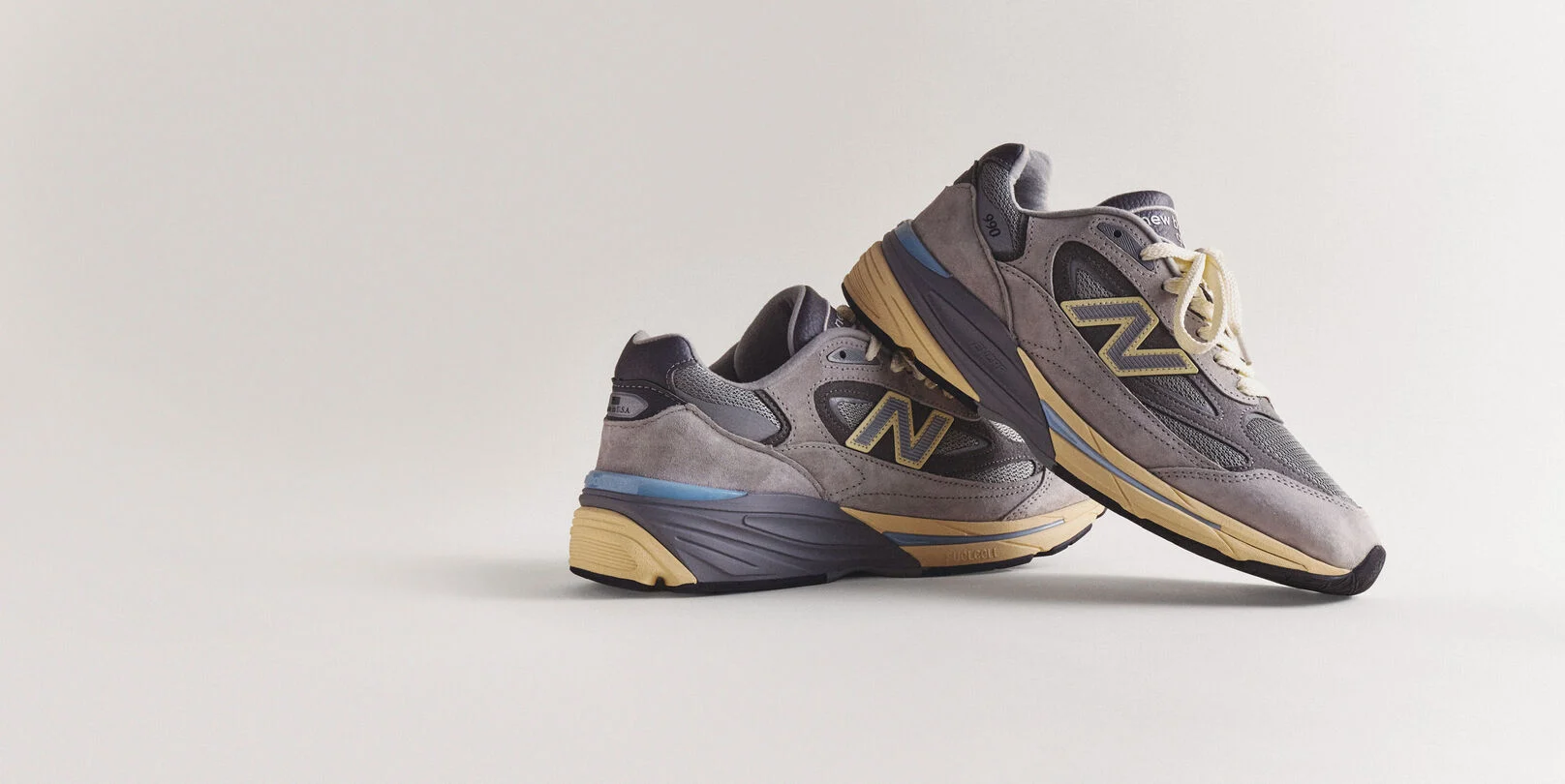A pair of grey 990v7 sneakers sitting on a grey studio backdrop.